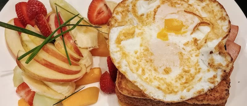Croque Madame, grilled ham and cheese French toast topped with a fried egg, served with fresh fruit